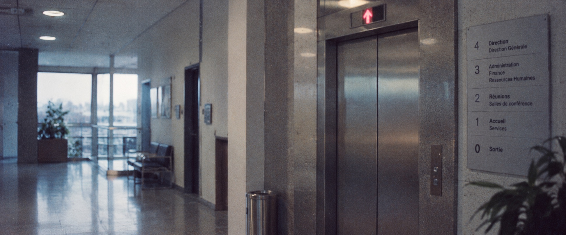 Kühler Büroflur mit Aufzug und französischem Wegweiser zu den Hierarchieebenen